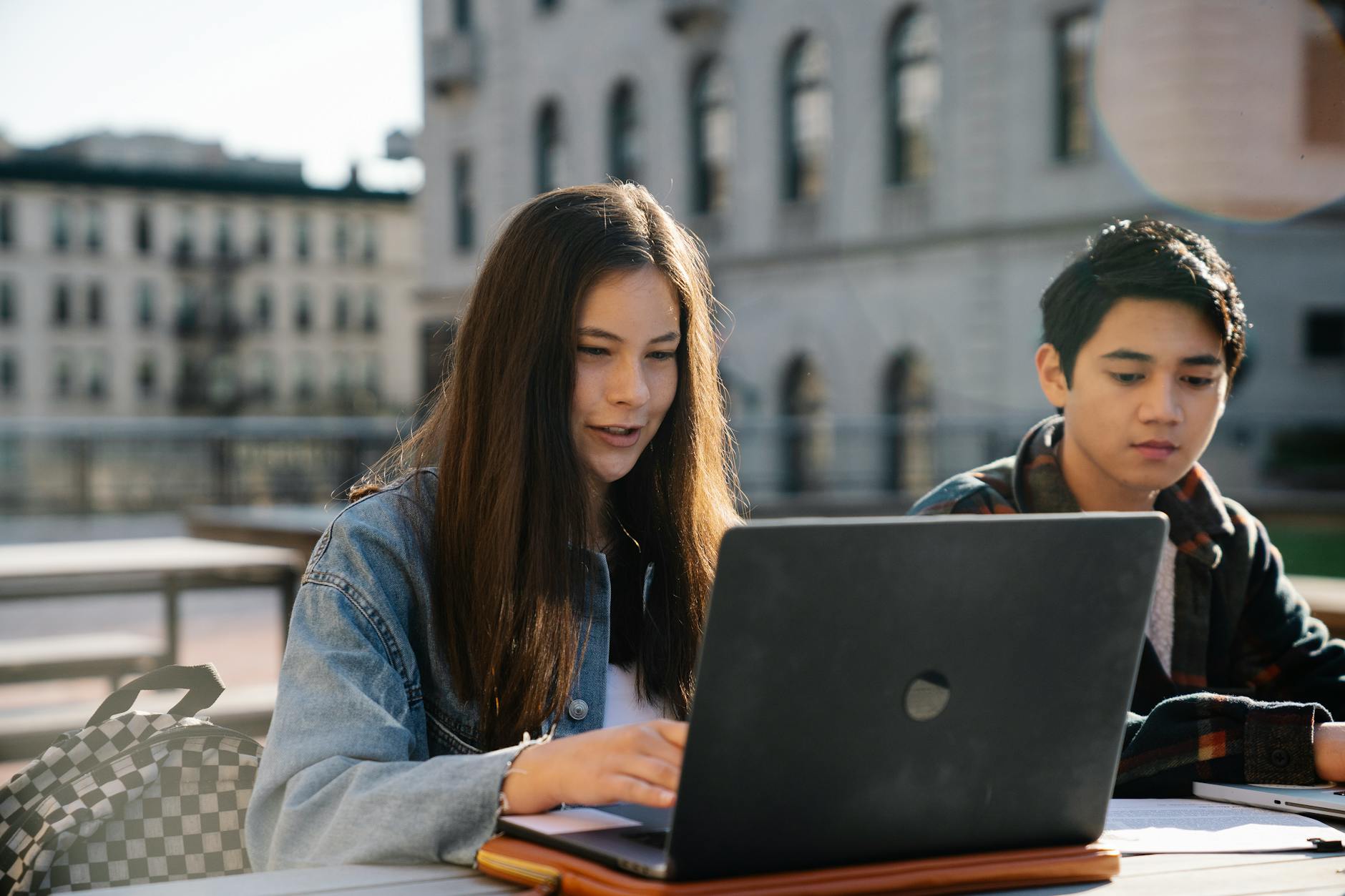 Dwójka uczniów gimnazjum korzysta z laptopa przed zabytkowym budynkiem
