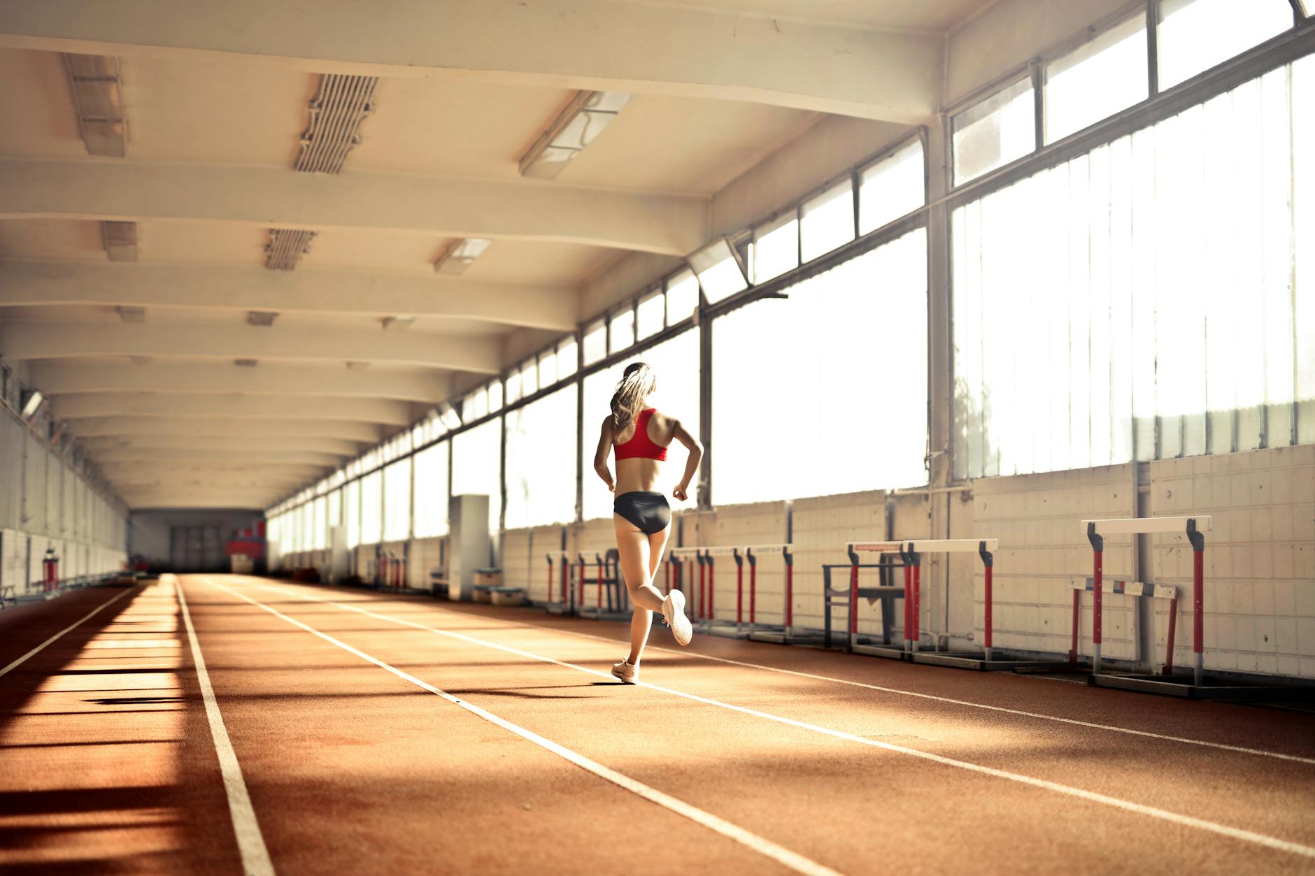 Biegaczka w stroju sportowym biegnie szybko po krytej bieżni Biegaczka w stroju sportowym biegnie szybko po krytej bieżni