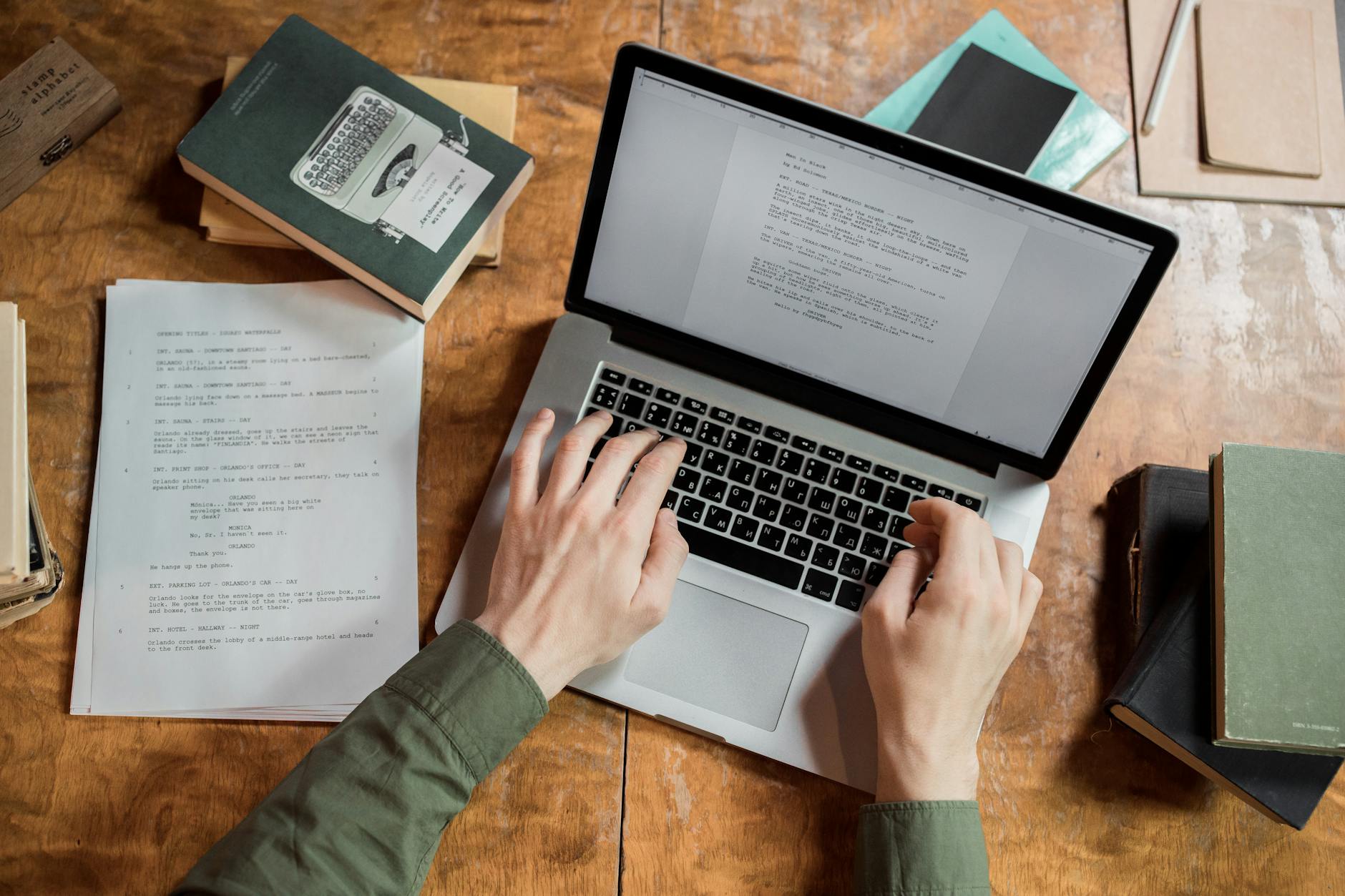 Osoba pisze na laptopie, wokół rozłożone książki i notatki