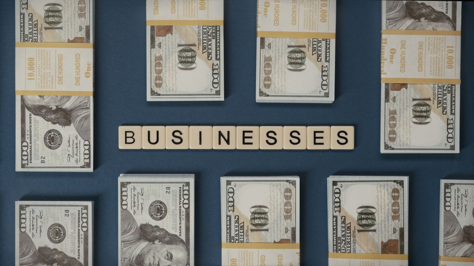 Plikające banknoty 100 dolarów i kostki Scrabble układające się w businesses