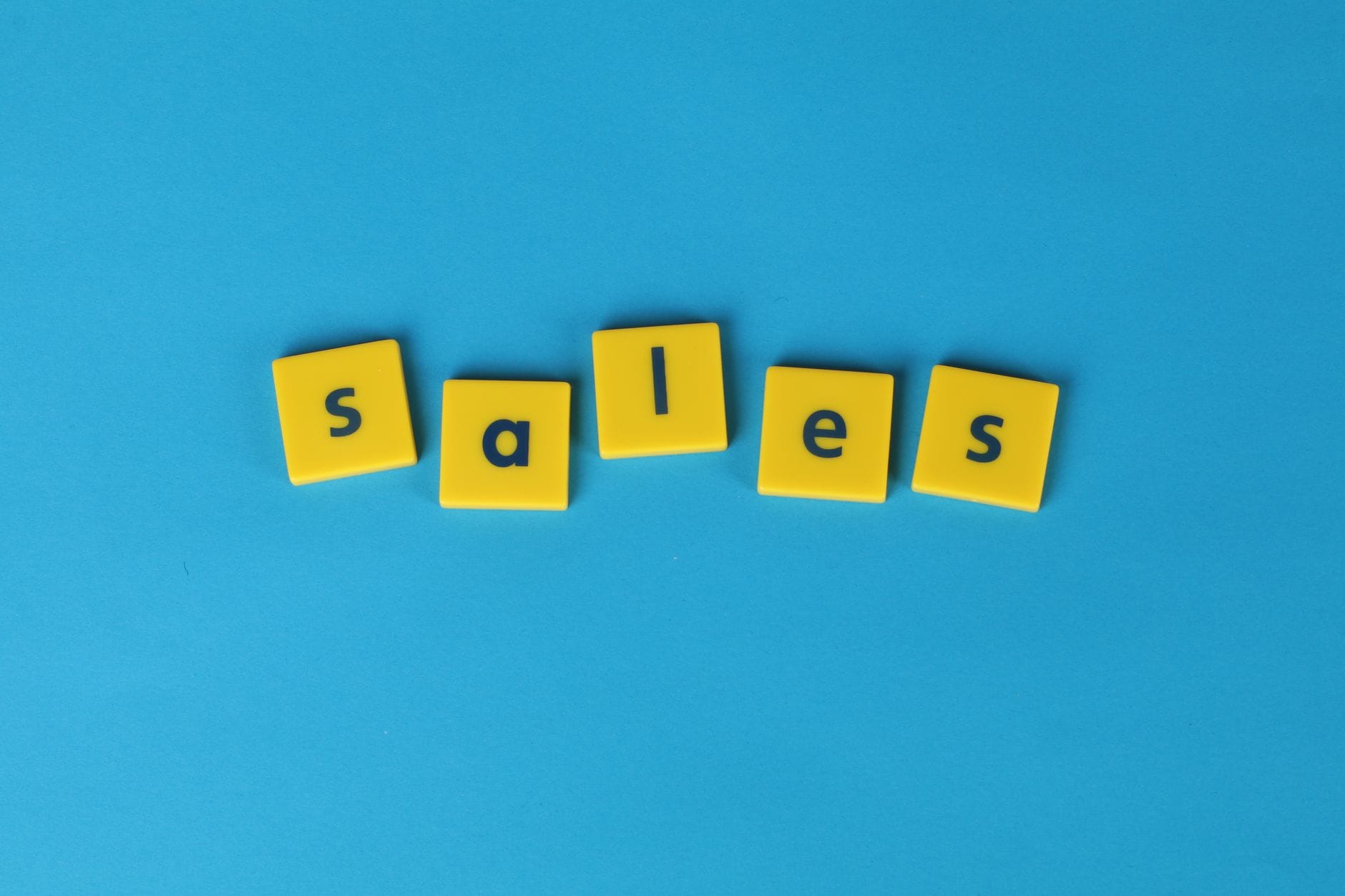 Żółte kafelki scrabble układające się w słowo sales na niebieskim tle