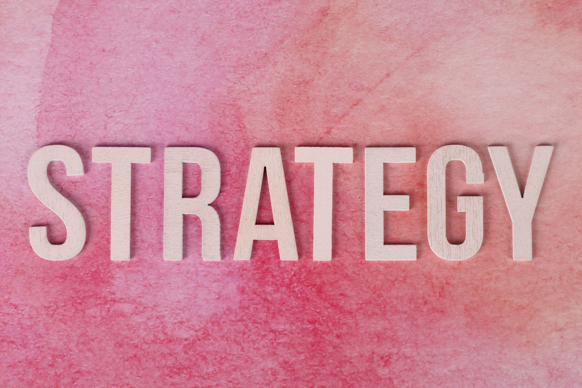 Drewniany napis Strategy na różowym tle nawiązuje do modelu biznesowego
