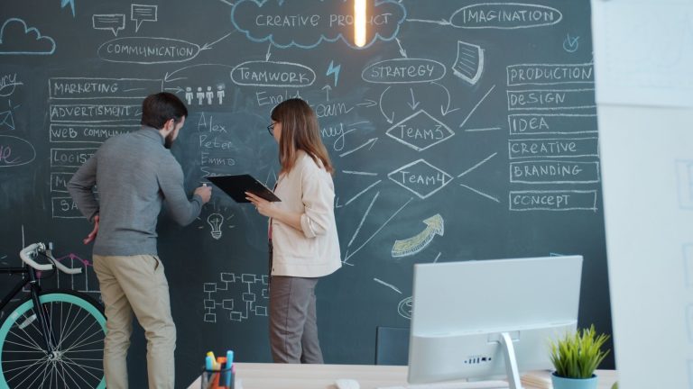 Dwoje współpracowników omawia strategię przy tablicy w biurze